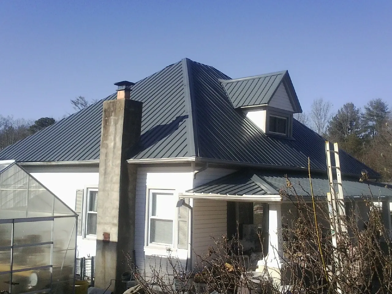 Dark blue standing seam metal roof on a white farmhouse with dormer — Slate & Tile Roof Repair by Roofing Brothers in Independence