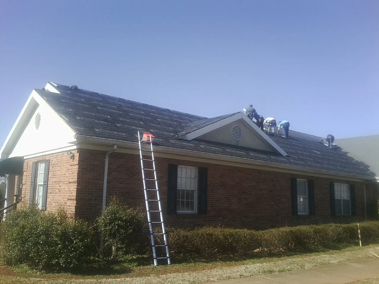 Crew tearing shingles off a brick ranch roof with a ladder set — Metal Roof Repair work by our crew in Independence
