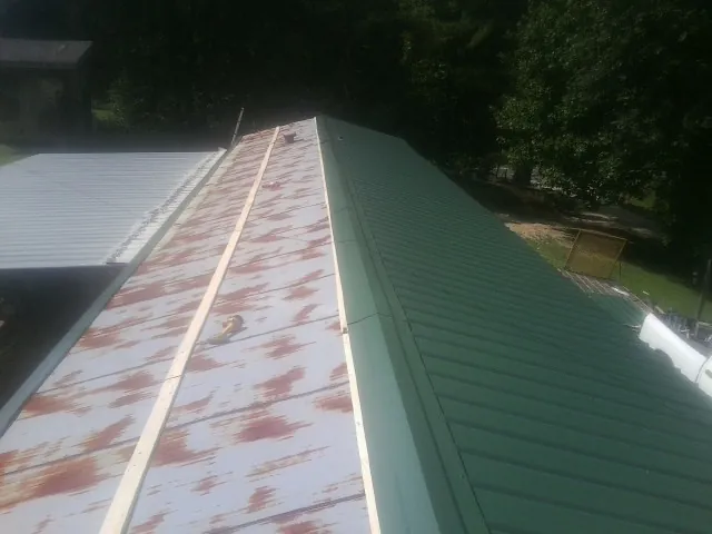 Old rusted panels beside newly installed green metal roofing — Wind Damage Roof Repair by Roofing Brothers in Independence