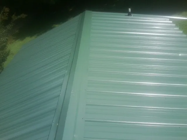 New green metal panels meeting at the ridge of a roof — Flat Roof Repair work by our crew in Independence